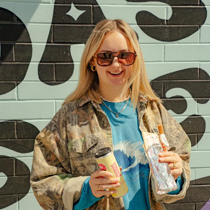 Customer holding a purchase in front of the Coastal Green mural
